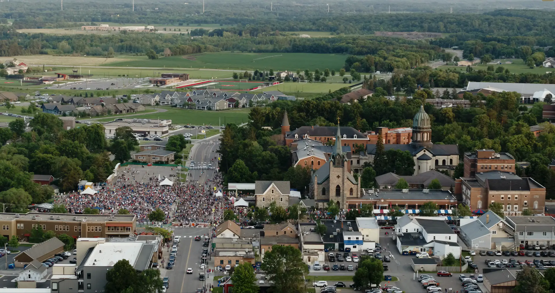 Downtown St. Joseph from the air at dusk, a crowd filling the street beside the church for a summer evening event.